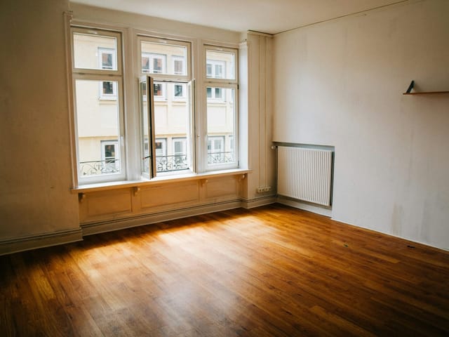 Leerer Altbauraum mit Holzboden und großen Fenstern