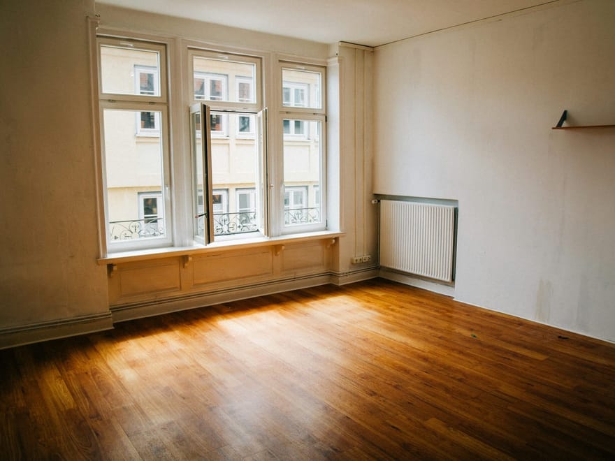 Leerer Altbauraum mit Holzboden und großen Fenstern