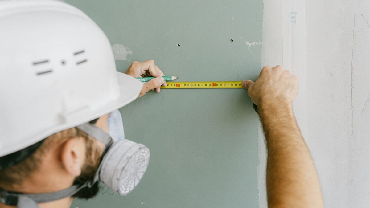 Handwerker mit Helm misst eine Gipskartonplatte mit dem Bandmaß aus