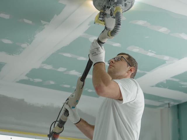 Handwerker schleift eine abgehängte Gipskartondecke