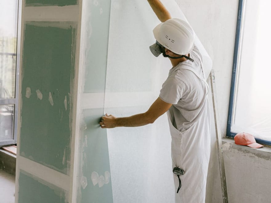 Handwerker mit Schutzhelm richtet eine Gipskartonplatte an einer Trockenbauwand aus
